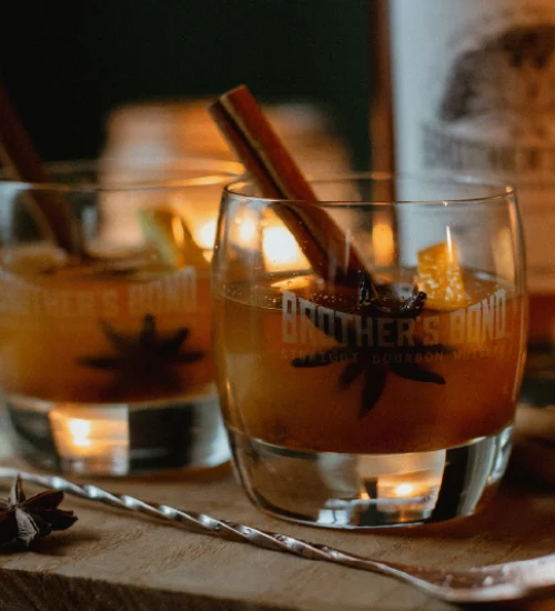 Verre de whisky de la marque The Brother's Bond Bourbon rempli de whisky avec en fond leur bouteille